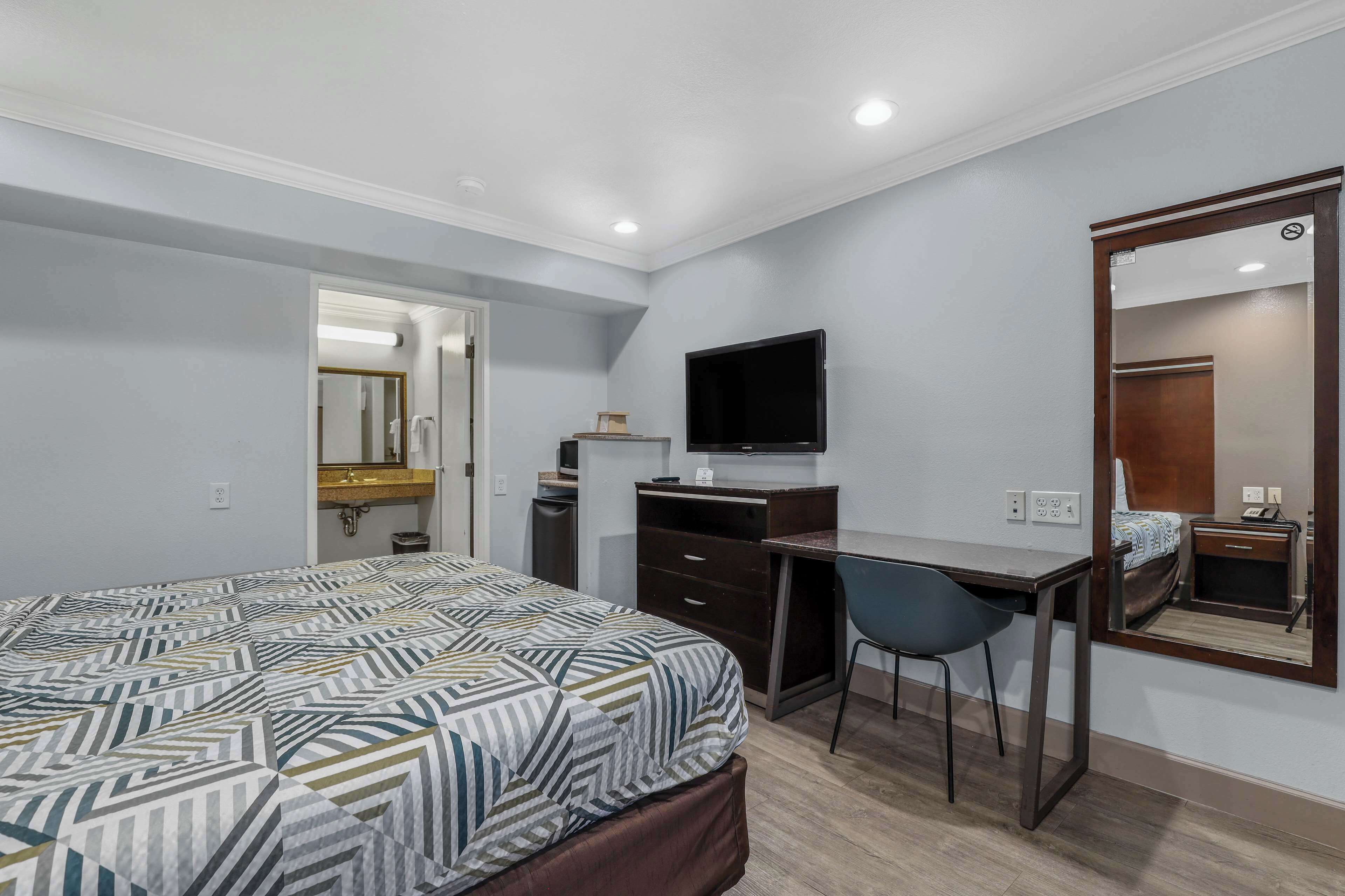 A hotel room with a bed, a desk, a chair, a television, and a mirror.