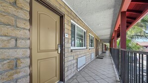 A covered corridor with a beige door, windows, and a tiled floor.