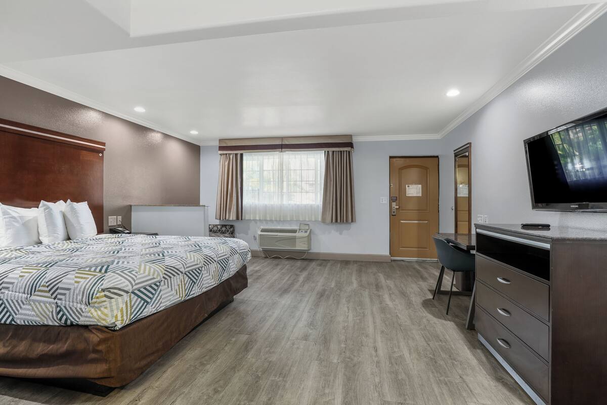 A hotel room with a bed, desk, dresser, TV, and an air conditioning unit.