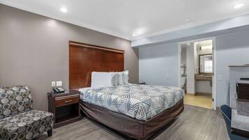 A hotel room with a bed, a chair, a nightstand, and a bathroom visible through an open door.