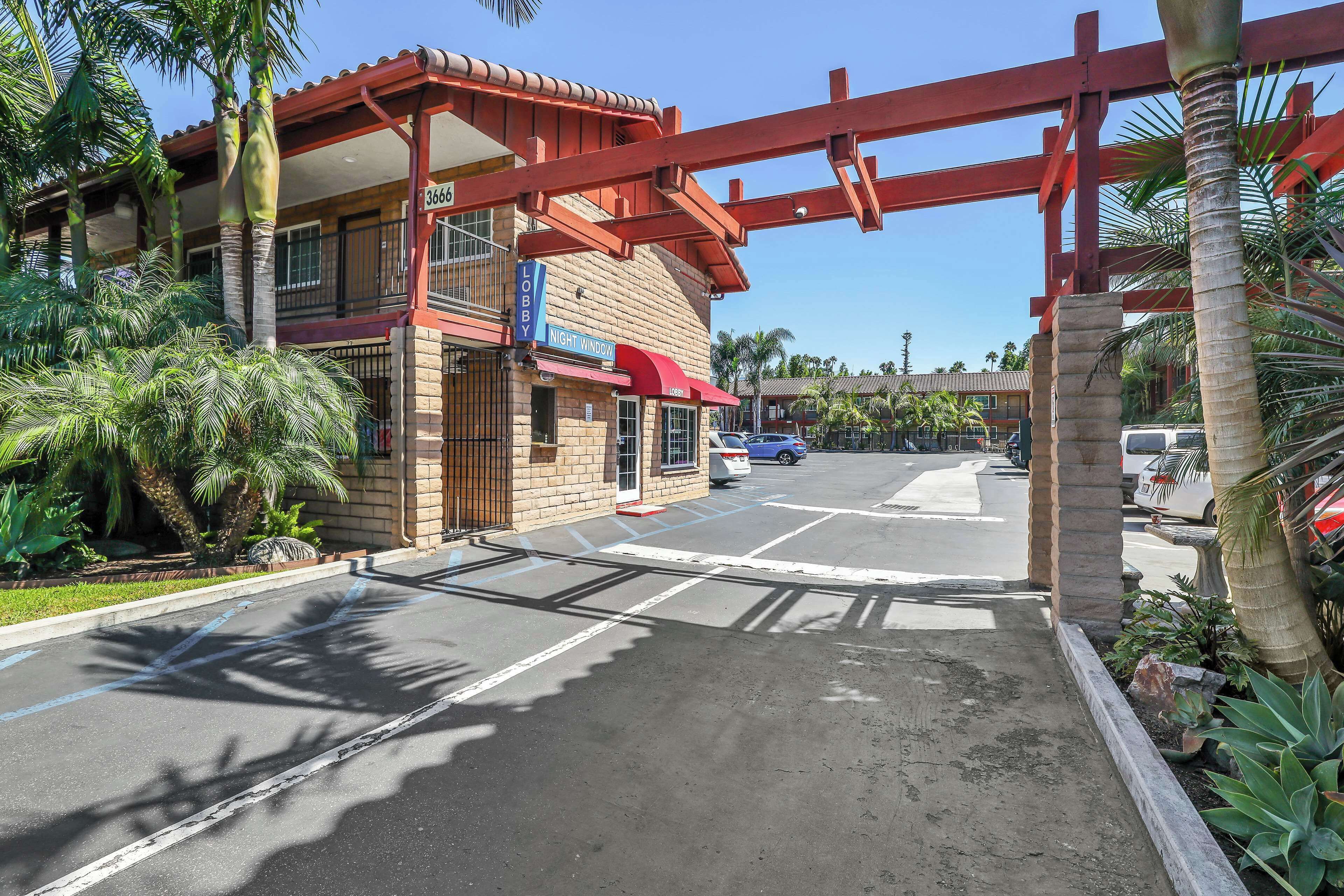 A hotel entrance with a red archway, a sign for the Night Window, and a parking lot with cars.