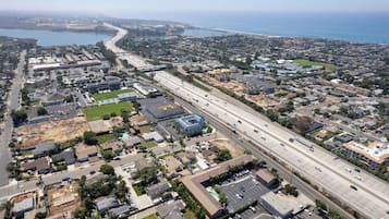 An aerial view of a coastal residential area with a main road, houses, and a large body of water in the background.