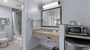 Un baño con inodoro, ducha, lavabo y un microondas en la encimera.