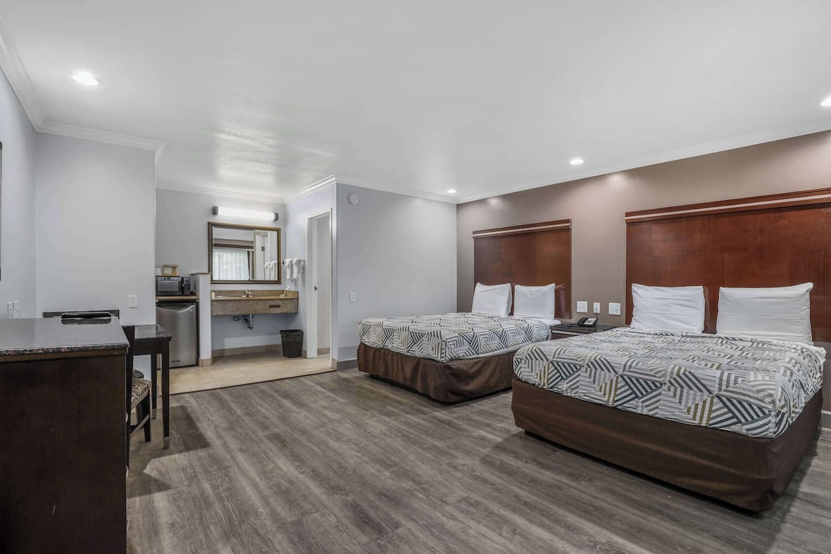 A hotel room with two beds, a desk, a mirror, and a small kitchenette.
