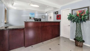 A reception desk with a dark wood finish, a potted plant to the right, and a framed picture above the door.