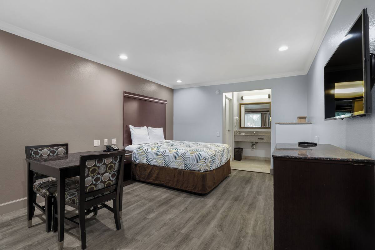 A hotel room with a bed, a desk with a chair, a dresser, and a mirror.