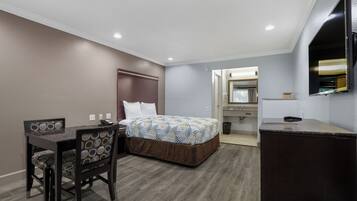 A hotel room with a bed, a desk with a chair, a dresser, and a mirror.