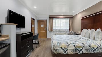 Una habitación de hotel con cama, escritorio, televisor y ventana con cortinas.