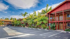 A hotel with a red facade, multiple balconies, and a parking lot with palm trees.
