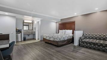 A hotel room with a bed, a sofa, a desk, and a kitchenette.