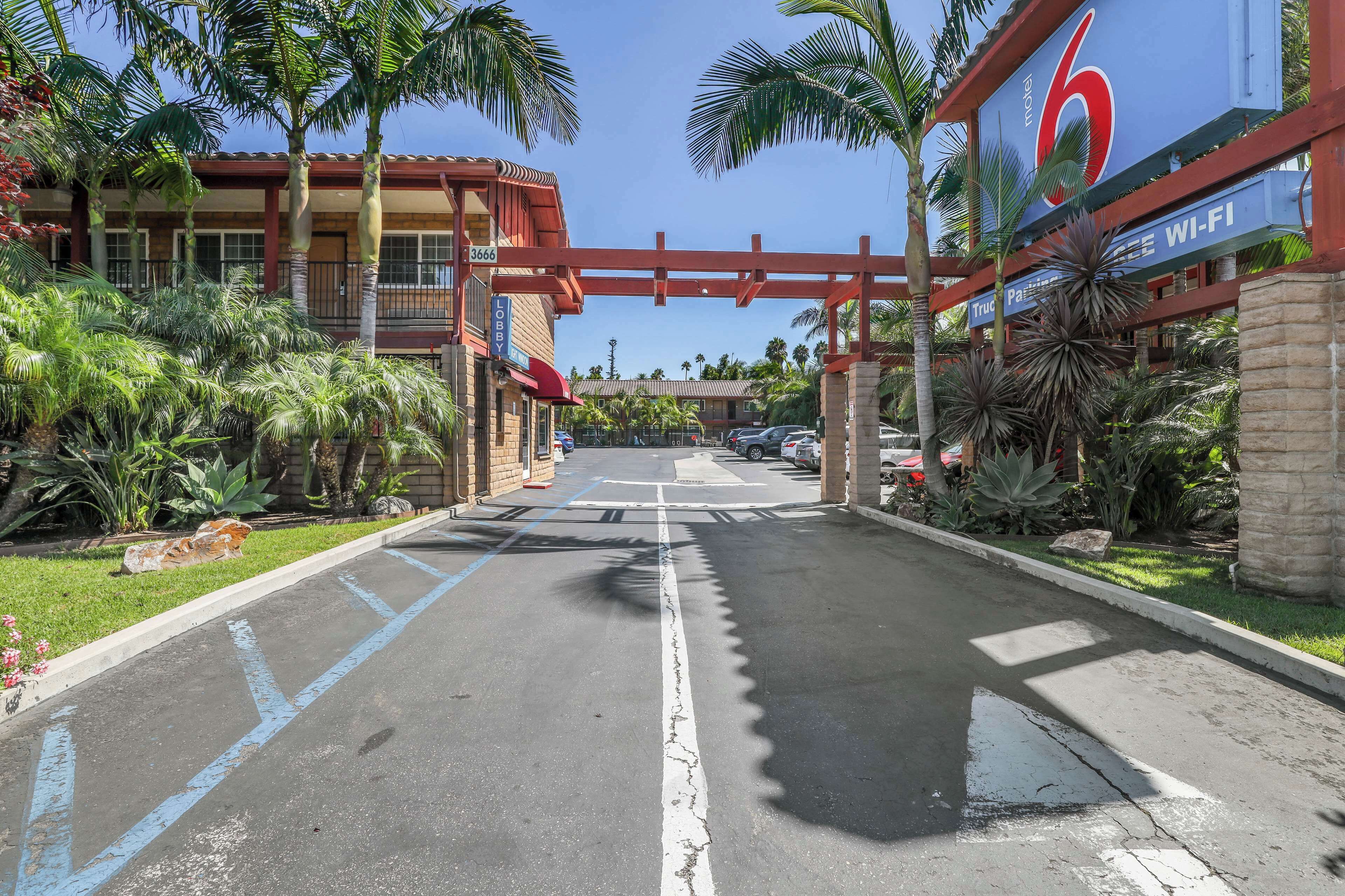 A hotel entrance with a red archway, palm trees, and a sign indicating 6 rooms and Wi-Fi availability.