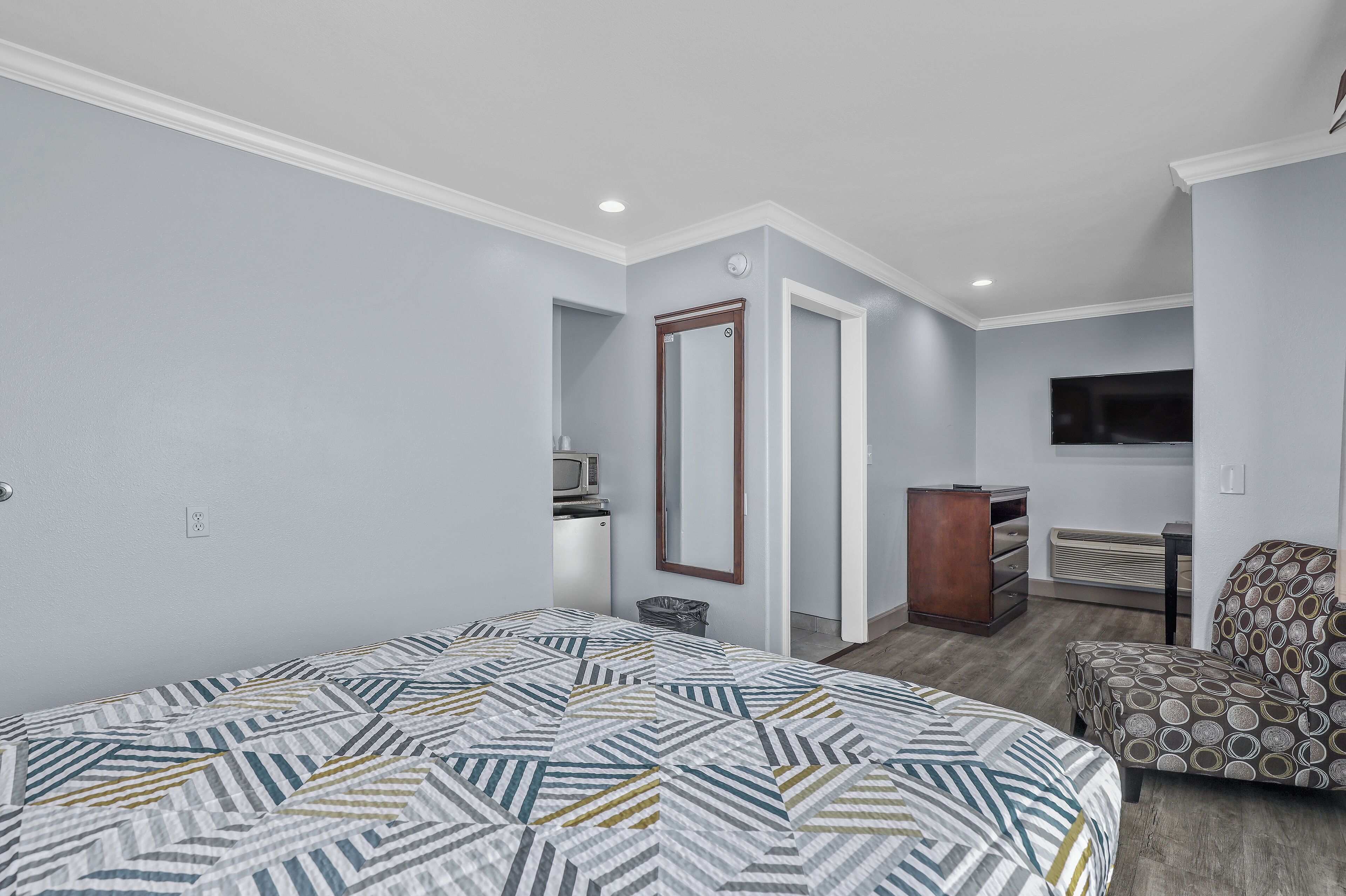 A bedroom with a bed, a dresser, a chair, a TV, and a microwave.