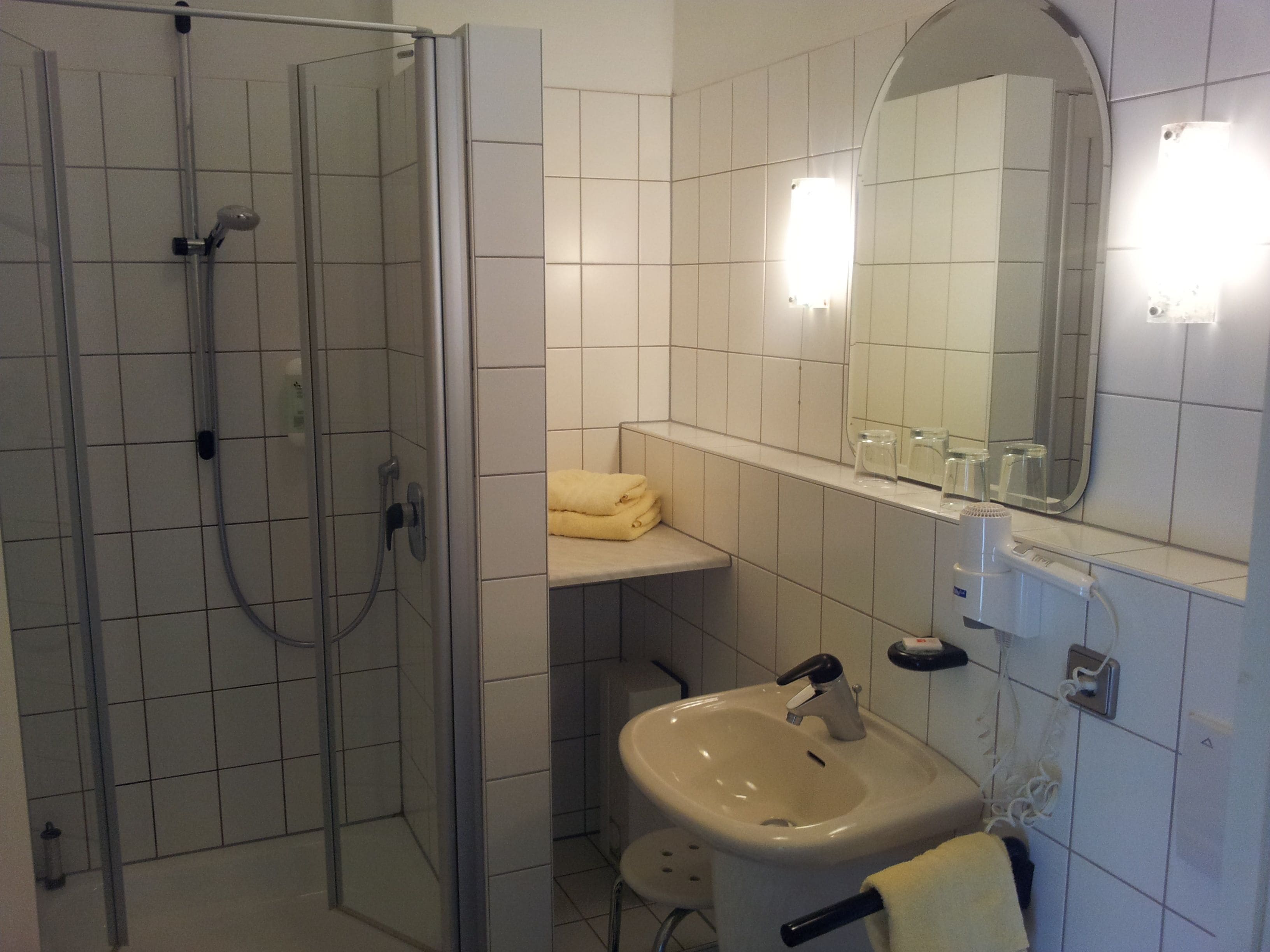 A bathroom with a glass-enclosed shower, a sink, a mirror, and a towel rack.