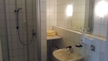 Un baño con ducha envuelta en cristal, un lavabo, un espejo y un perchero para toallas.