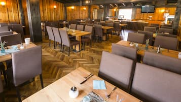Ein Restaurant mit Holzwänden und Fischgratparkett, das mehrere Esstische und Stühle bietet.