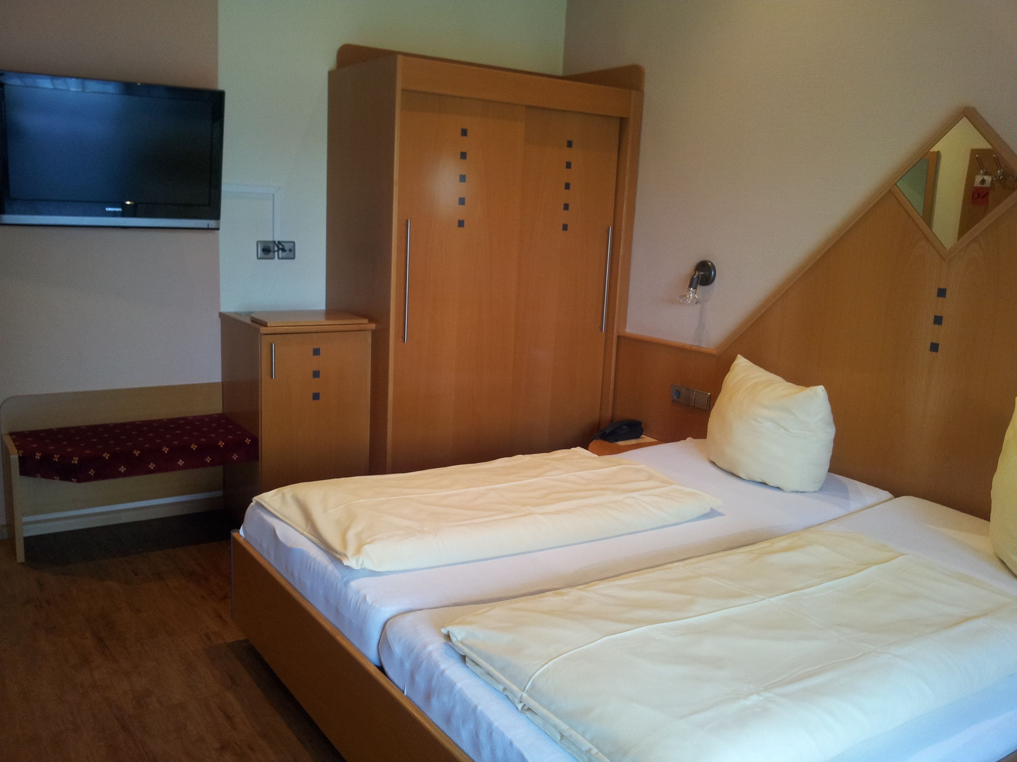 A hotel room with two beds, a wardrobe, a TV, and a bedside table.