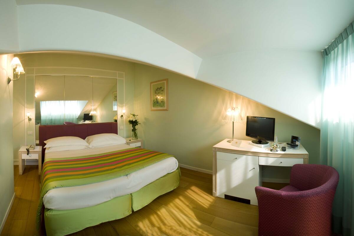 A hotel room with a bed, desk, chair, and a television.
