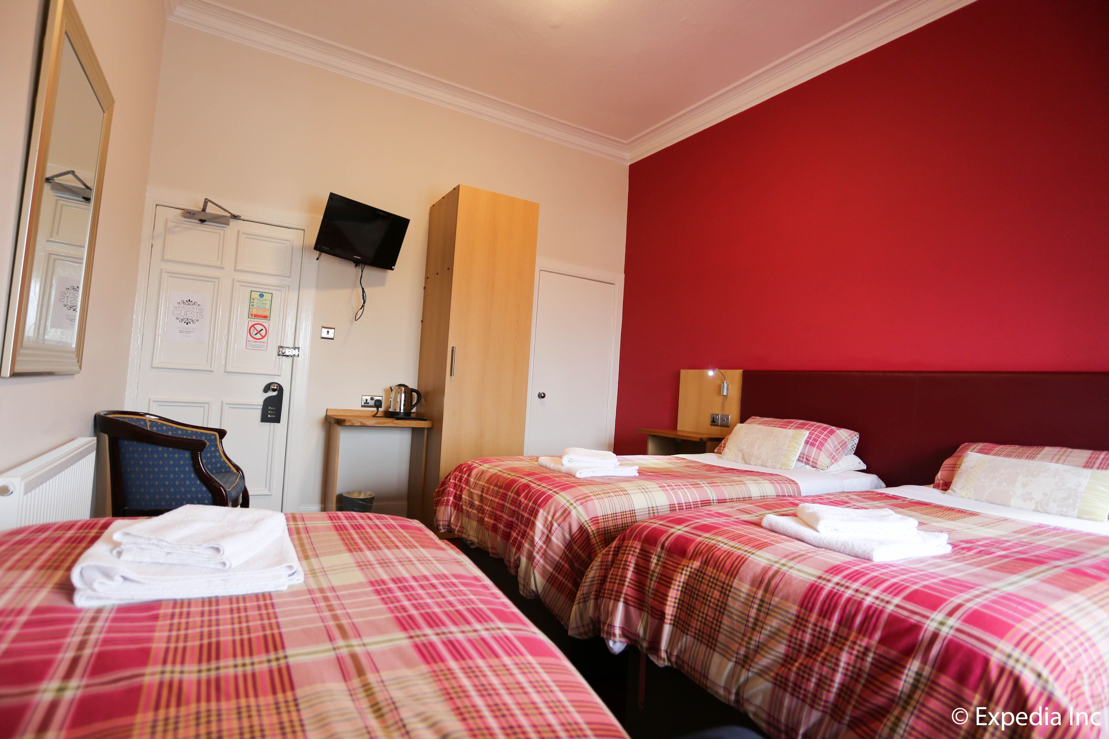 A hotel room with two beds, a television mounted on the wall, a wooden cabinet, and a red accent wall.