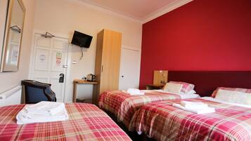 A hotel room with two beds, a television mounted on the wall, a wooden cabinet, and a red accent wall.