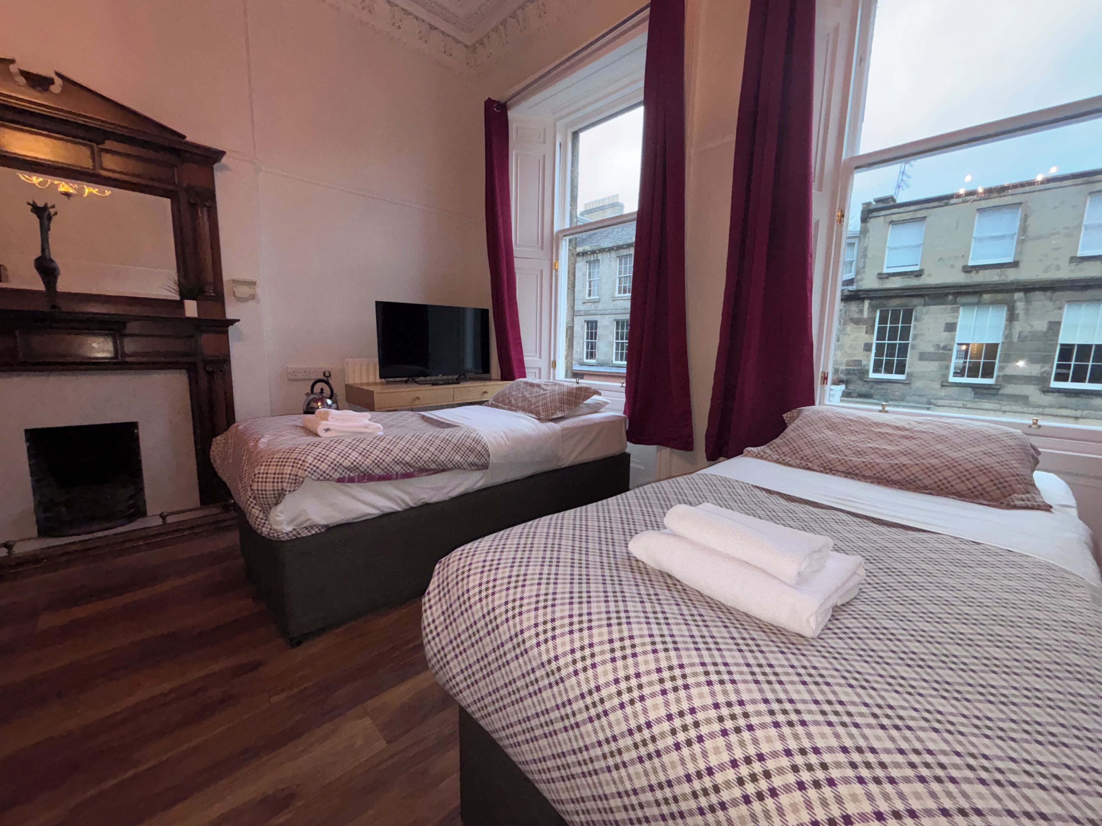 A hotel room with two beds, a television, a fireplace, and a view of buildings outside.