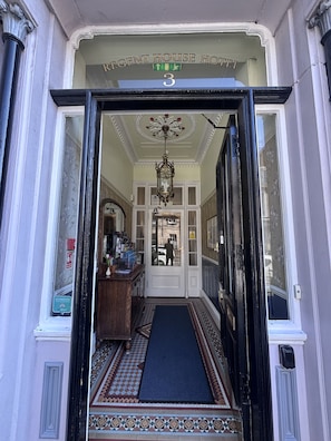 The entrance to Regent House Hotel with a black door, a blue mat, and a sign above the door.