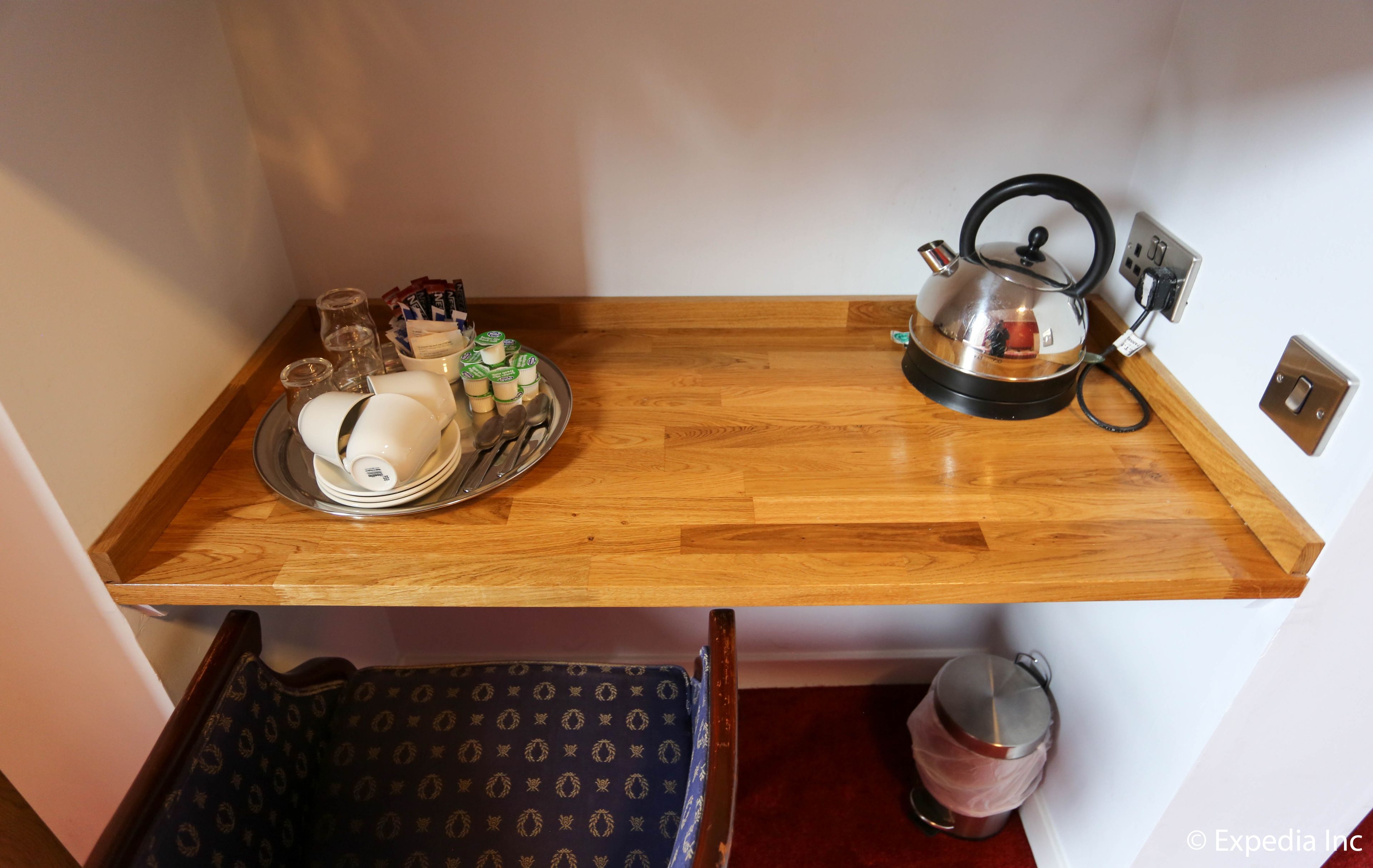A small kitchen area with a wooden countertop, a kettle, a tea set, and a mug.