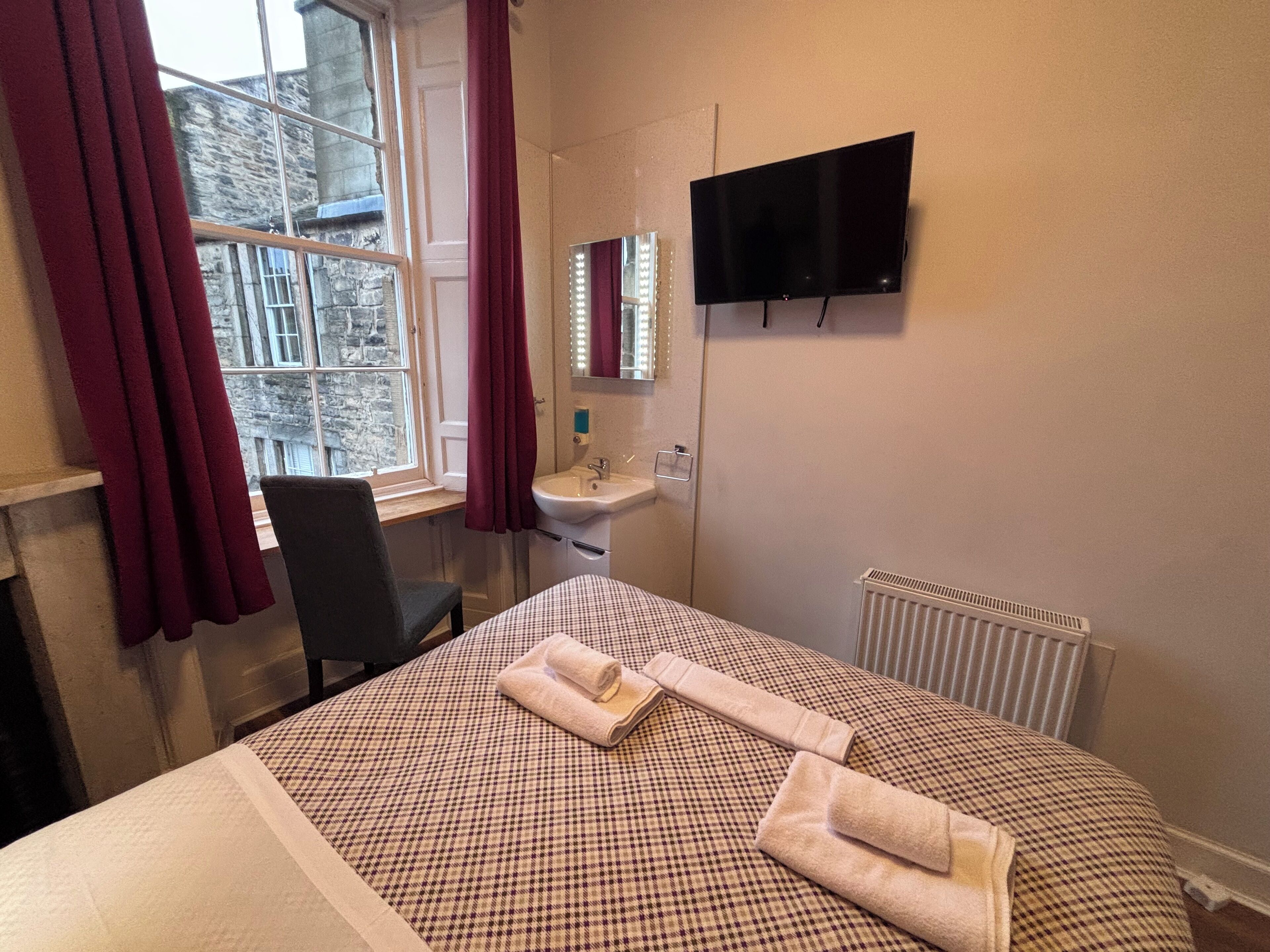 A hotel room with a bed, a desk, a sink, a mirror, and a TV.
