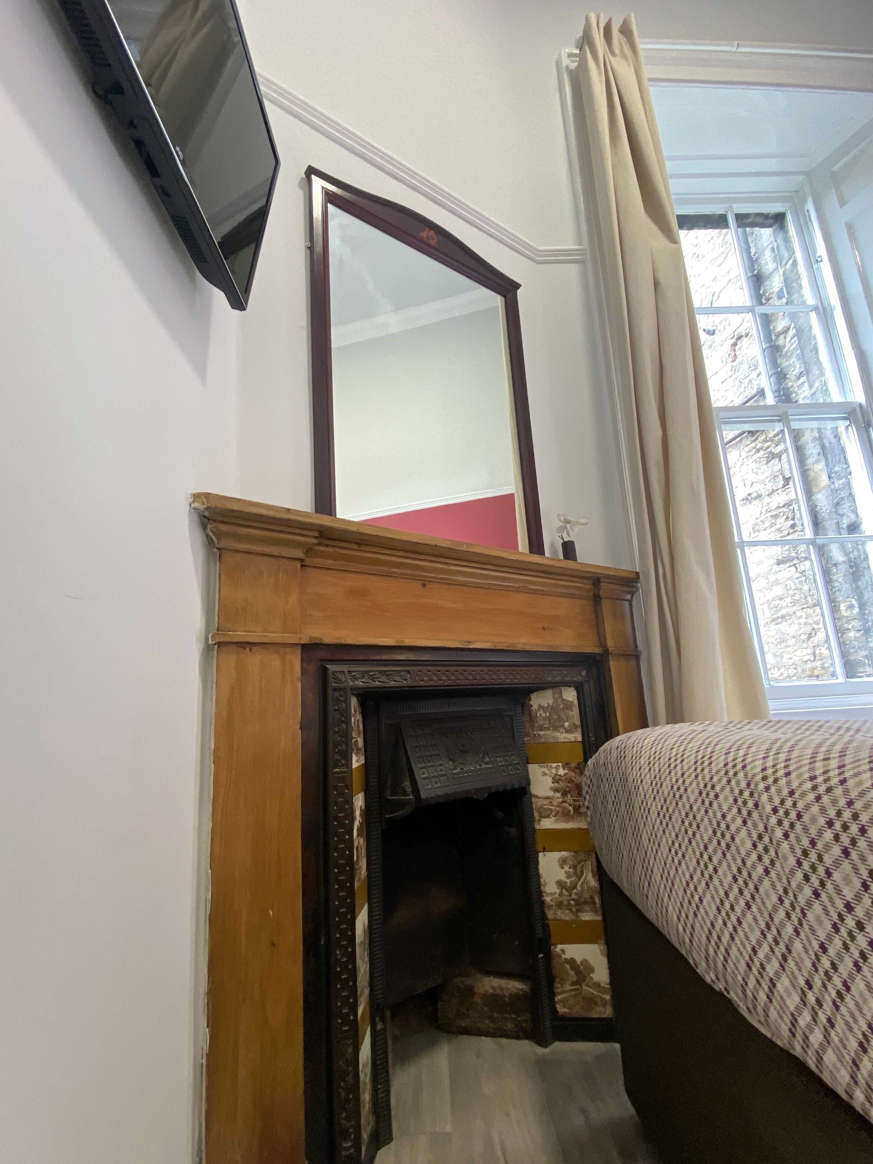 A bedroom with a bed, a fireplace, a mirror, and a window with curtains.