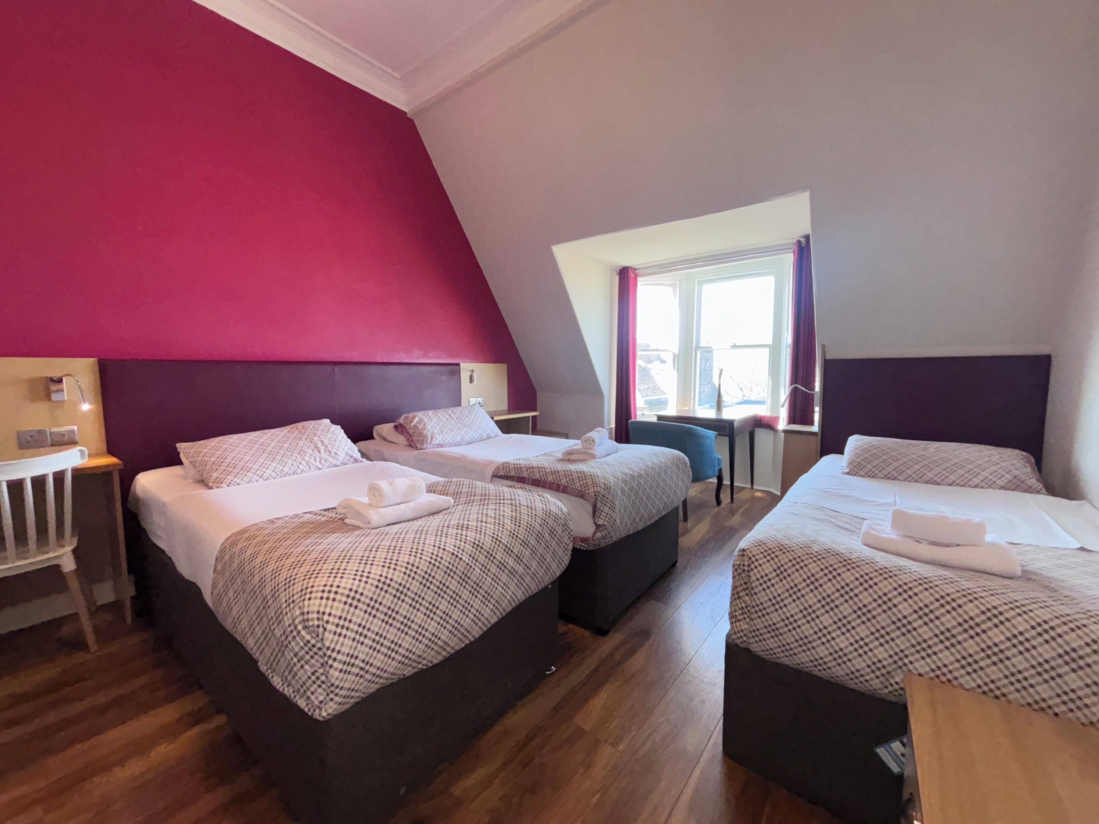 Habitación de hotel con dos camas, un escritorio y una ventana con cortinas.