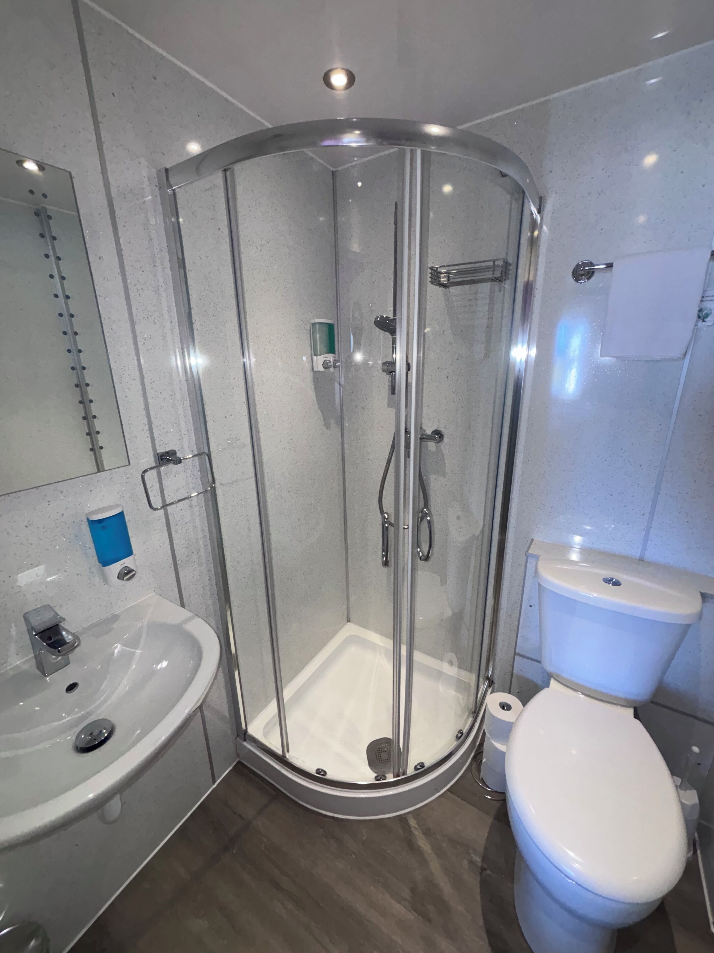 Een moderne badkamer met een douchecabine van glas, een witte wastafel en een toilet.