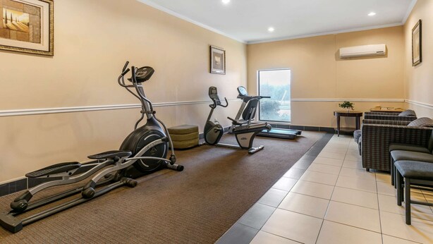 Un espace dédié à la remise en forme, équipé de vélos d’appartement et d’un tapis de course, un coin salon avec des canapés et une petite table, ainsi qu’une grande fenêtre offrant une vue sur l’extérieur.