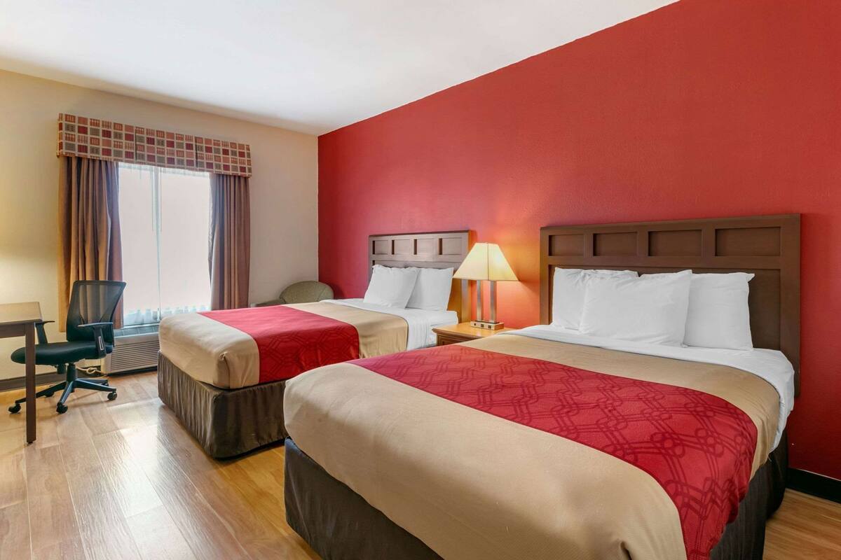 Habitación de hotel con dos camas, un escritorio, una silla y una ventana con cortinas.