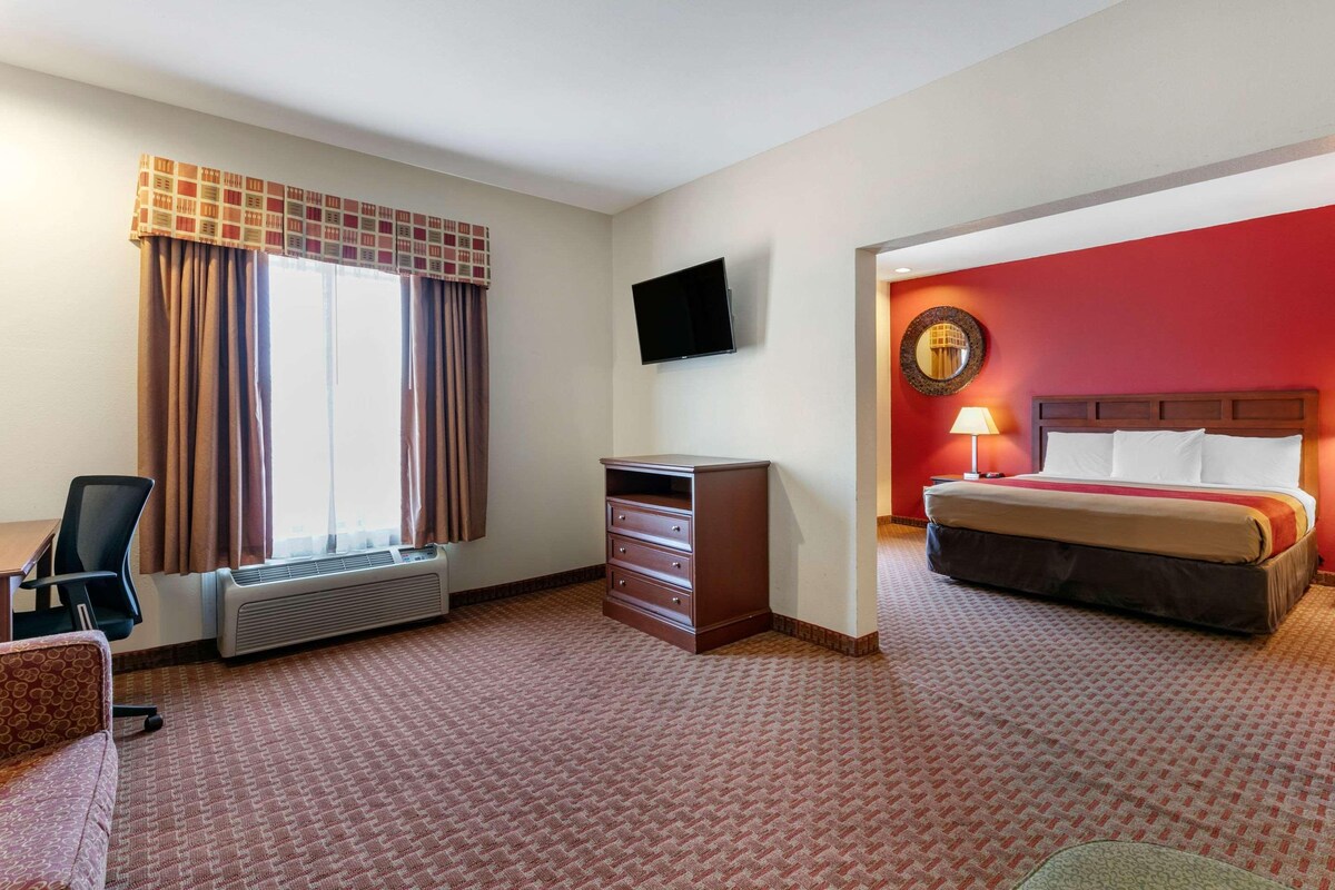 A hotel room with a bed, a desk, a chair, a dresser, a TV, and a window with curtains.