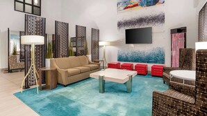 A modern living room with a beige sofa, a coffee table, and red ottomans. There is a TV mounted on the wall and decorative panels. - Best Western Plus Daphne Inn & Suites (Daphne)