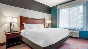 Una camera d'albergo con un letto grande, due comodini con lampade, una finestra con tende leggere e un condizionatore d'aria a parete.