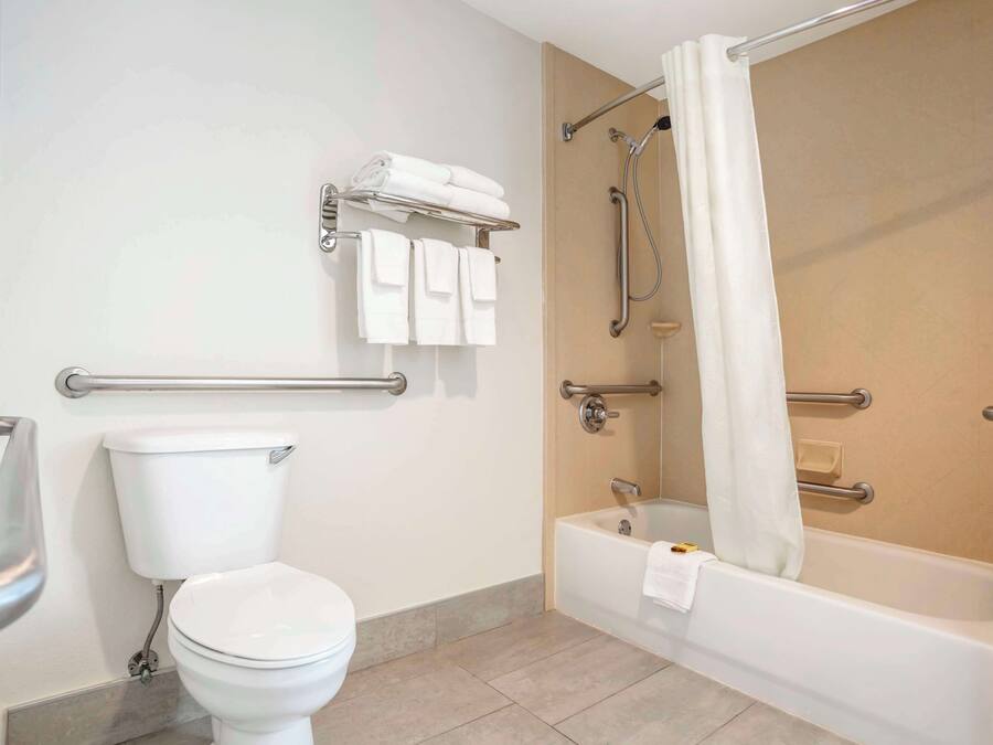 A bathroom with a toilet, a bathtub with a shower, and a handrail.