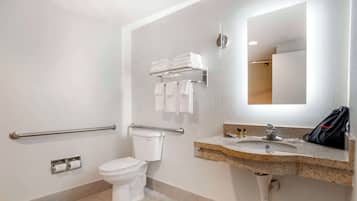 Een badkamer met een toilet, handgrepen, een wastafel met spiegel en een handdoekrek.