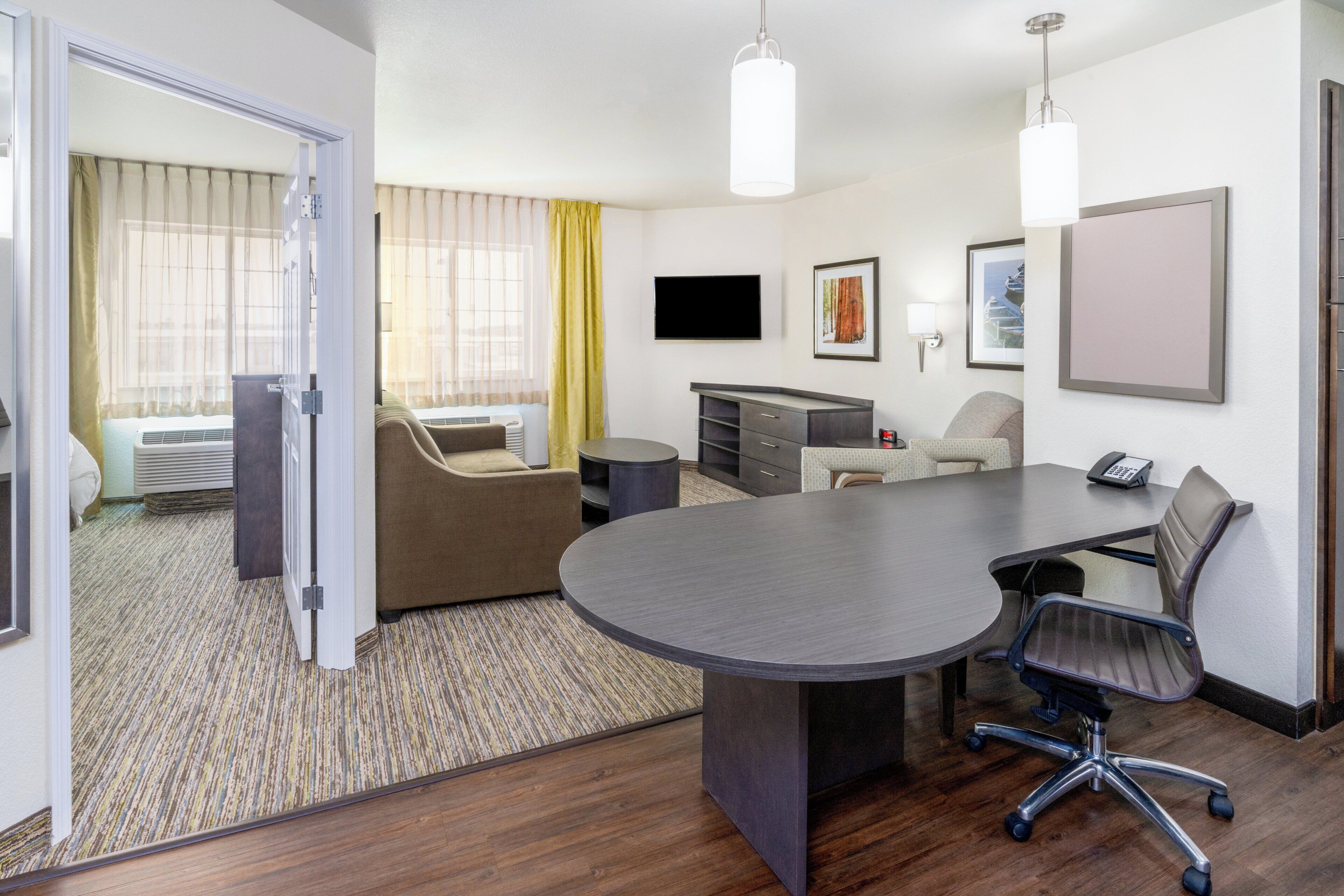 A hotel room with a large conference table, a sofa, a desk, and a television.