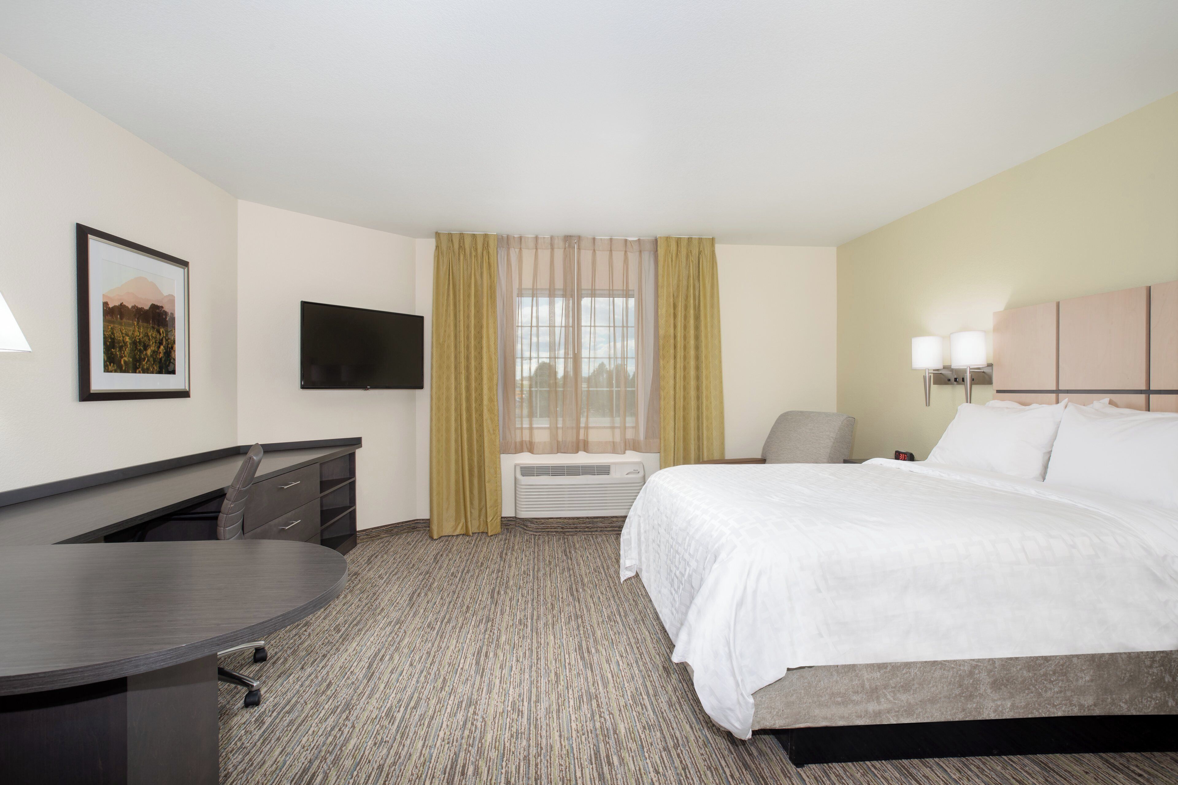 A hotel room with a bed, a desk, a chair, a TV, and a window with curtains.