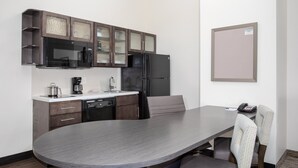A modern kitchen with dark wood cabinets, a black refrigerator, and a microwave. There is a dining table with two chairs and a coffee maker on the counter. - Candlewood Suites Cheyenne by IHG (Cheyenne)