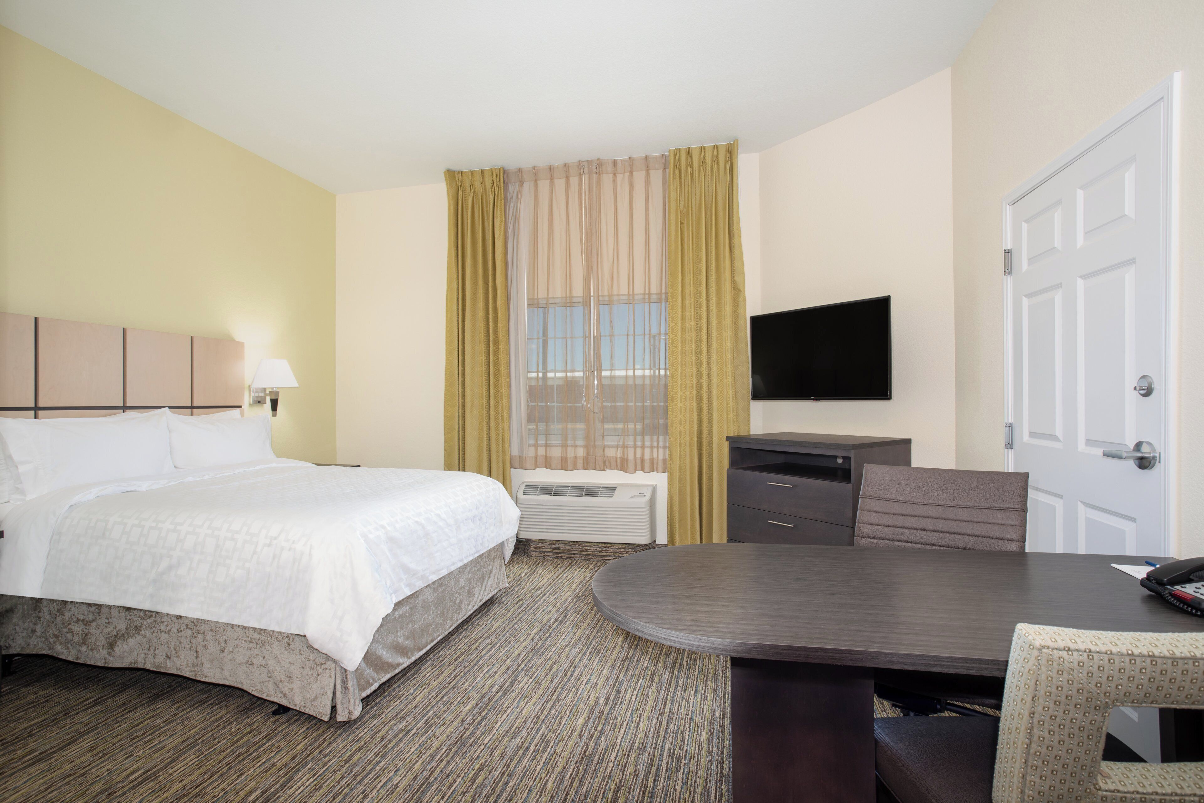 A hotel room with a bed, a desk, a chair, a television, and a door.