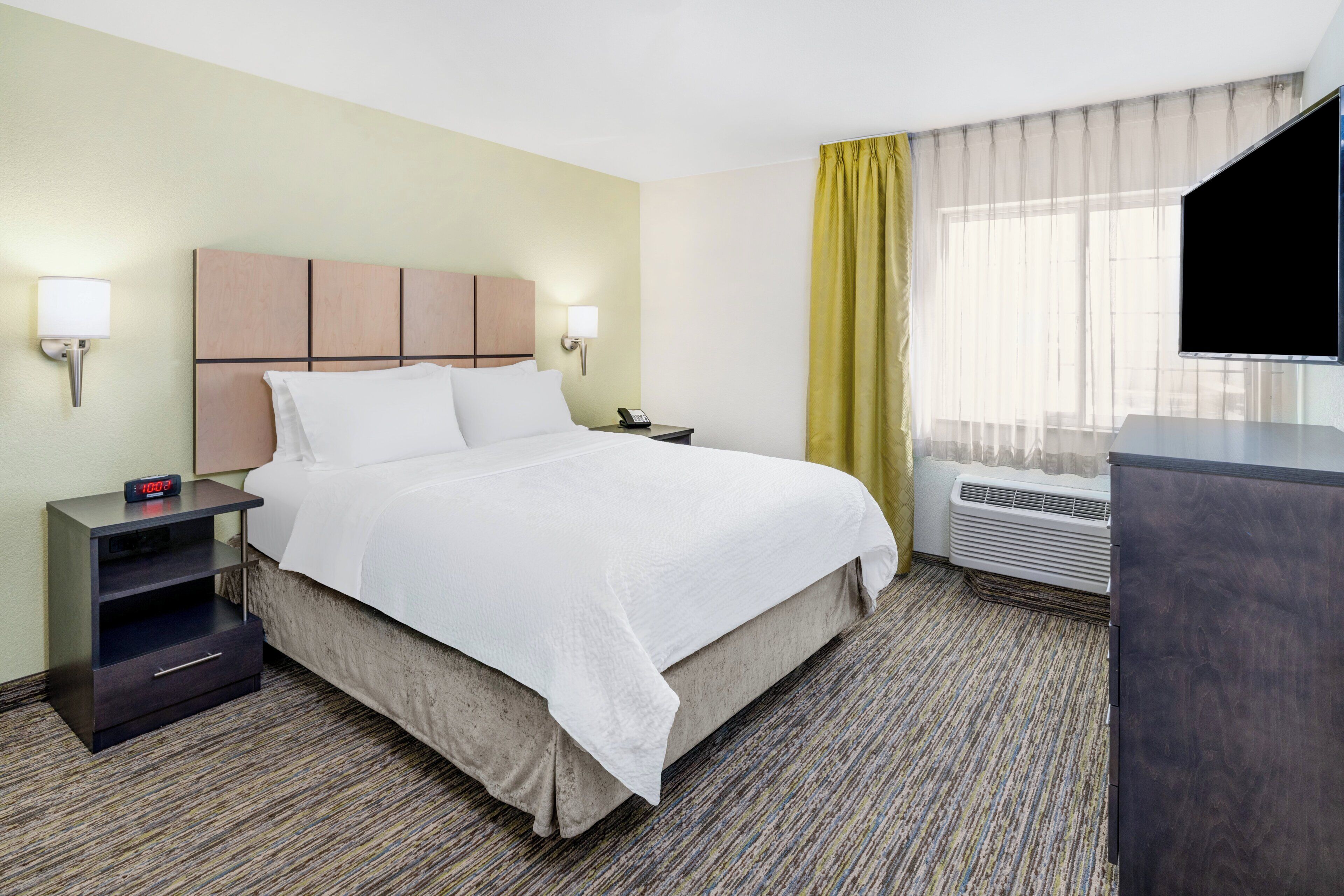 A hotel room with a bed, bedside tables, a TV, and a window with curtains.