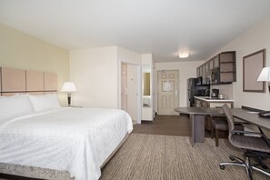 A hotel room with a bed, desk, chair, kitchenette, and a bathroom.