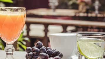 A table with a glass of orange juice, a bowl of grapes, a cup of water with a lime slice, and a white bowl.