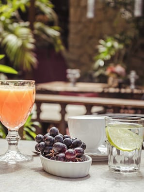 Una mesa con un vaso de jugo de naranja, un cuenco de uvas, una taza de agua con rodaja de lima y un cuenco blanco.