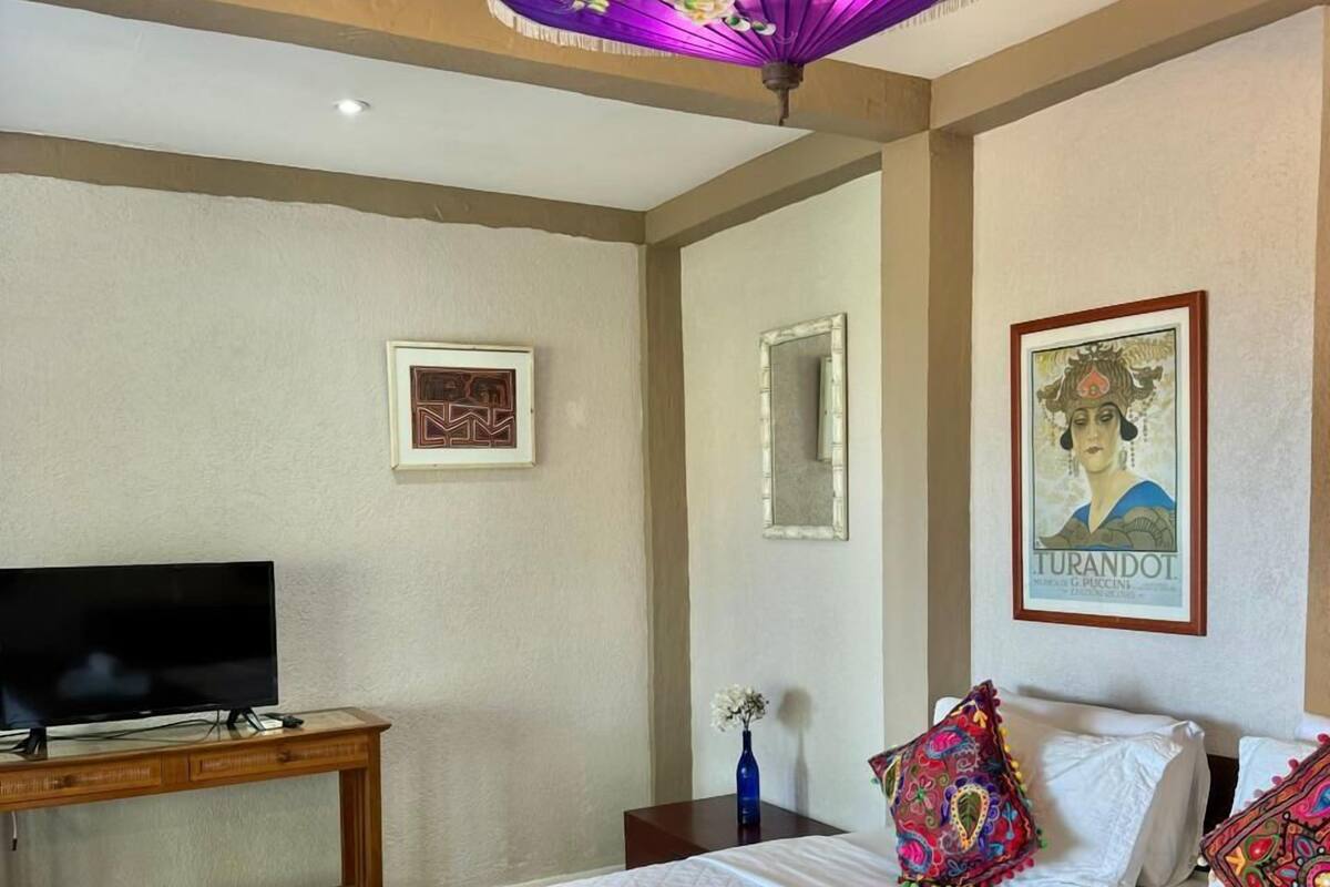 Una habitación de hotel con una cama, televisión, un paraguas decorativo y obras de arte en las paredes.