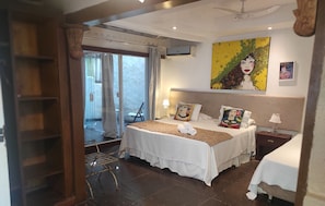 Una habitación de hotel con cama, mesita de noche, lámpara, un cuadro y una ventana con cortinas.