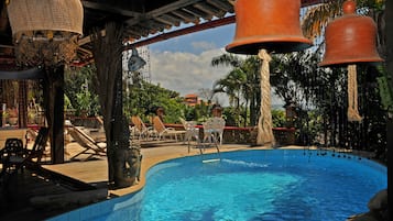 A pool area with lounge chairs, a decorative hanging bell, and a clear blue pool.