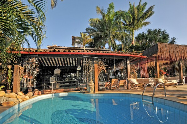 Un espace aménagé au bord de la piscine, comprenant un bar, des chaises longues et des palmiers.