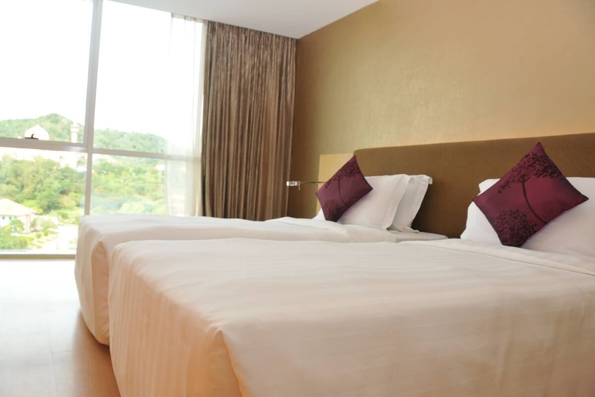 A hotel room with two beds, beige bedding, and a large window with curtains.
